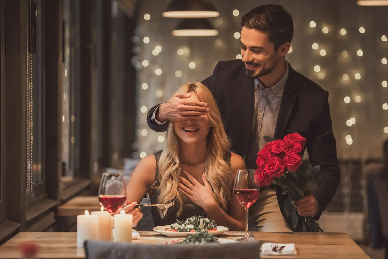 mężczyzna z kwiatami zasłania oczy kobiecie przy stole